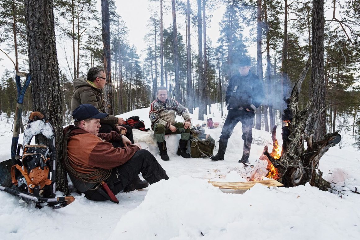 Finnland. Männer-Schutzgebiet 7 Gruppe sitzt um Lagerfeuer Winter Finnland